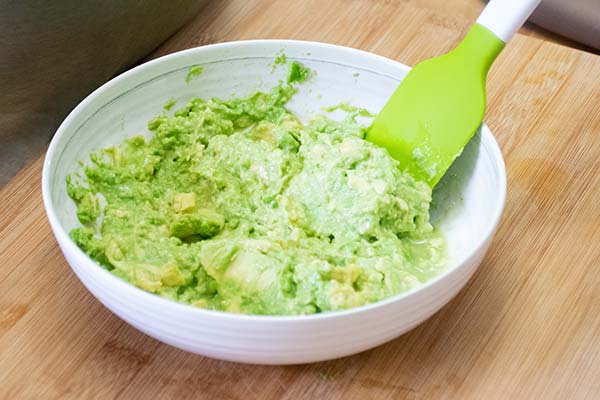 A bowlful of mashed avocado with a rubber scraper 