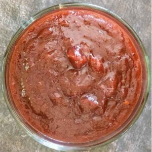 Overhead view of a glass bowl filled with dark red cranberry chipotle sauce on a textured gray surface.