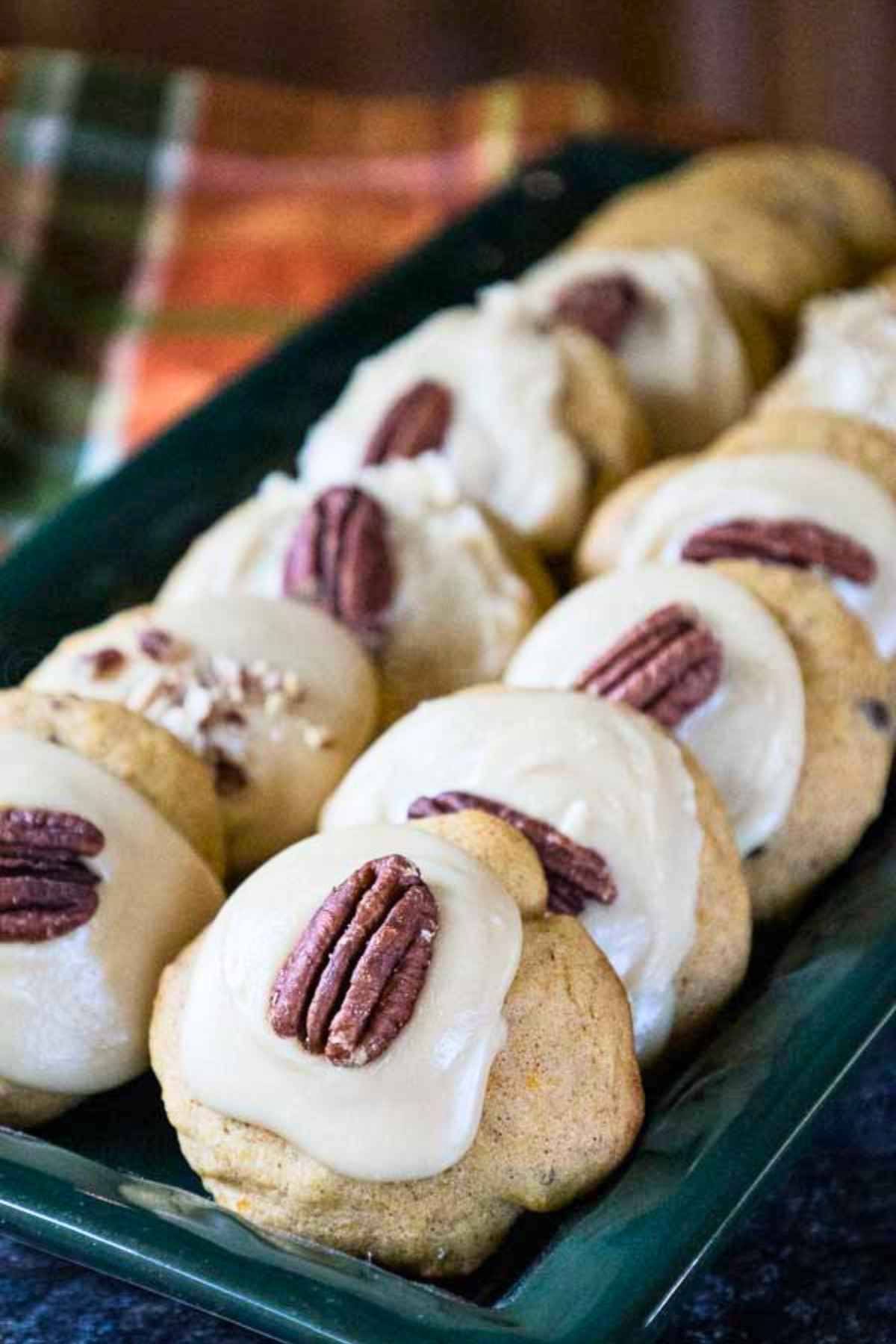 A green serving tray filled with frosted cookies each garnished with a pecan half.