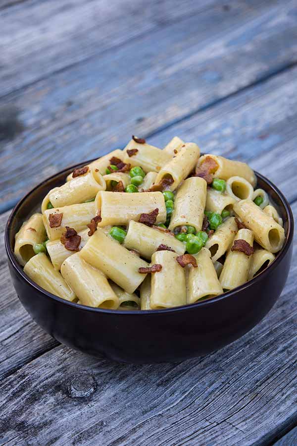 A bowl full One Pot Alfredo with bacon and peas.