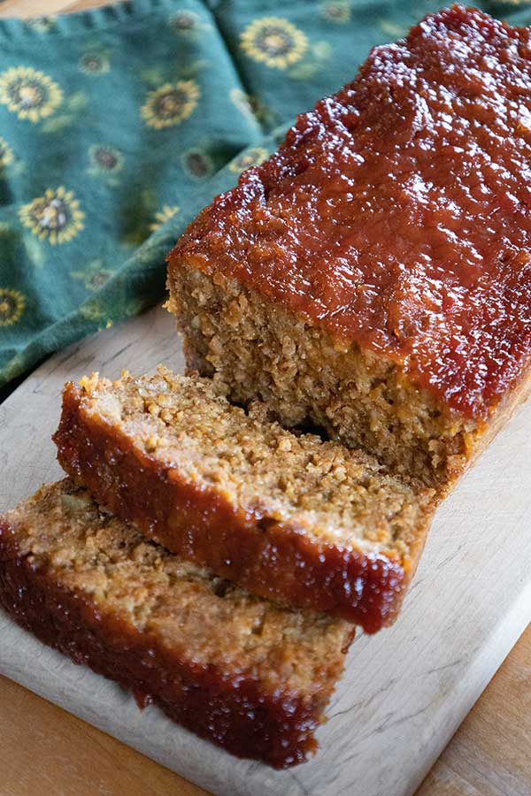 Vegetarian meatloaf on a cutting board with two slices cut from the loaf.