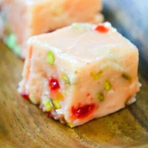 Plate of creamy eggnog fudge squares with cherries and pistachios.