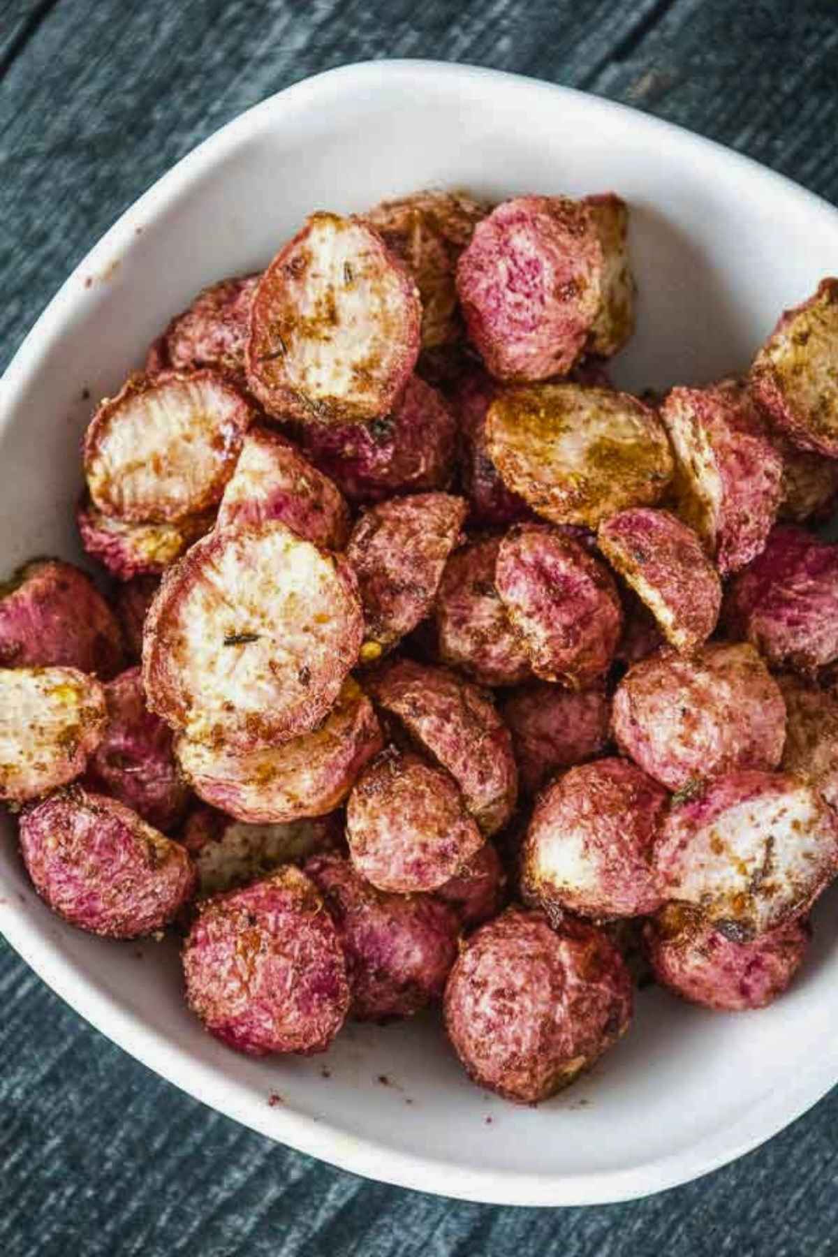 Close up image of a bowl full of roasted radishes with visible seasoning on them.