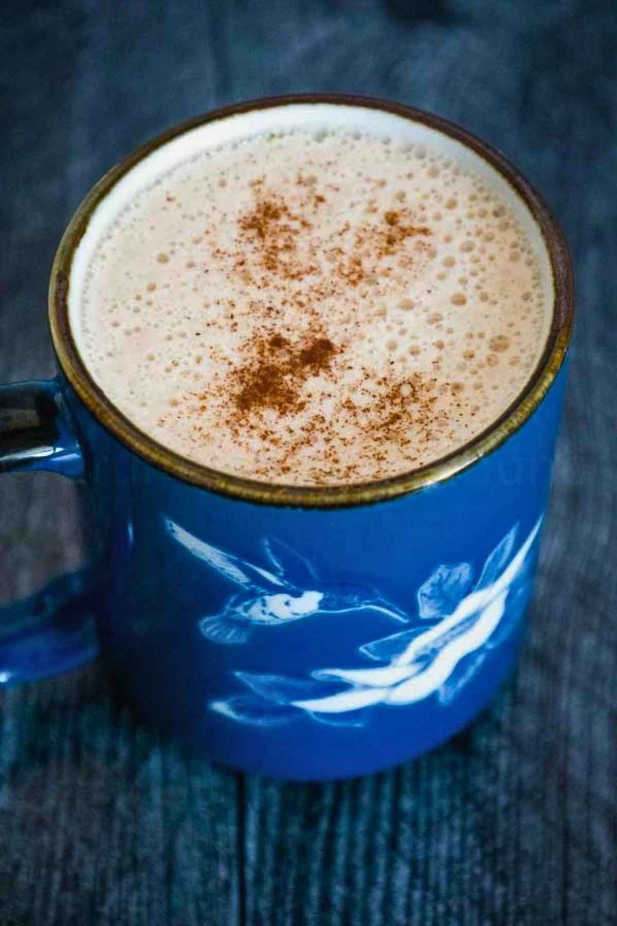 Close up of a foamy drink sprinkled with cinnamon in a blue hummingbird mug.