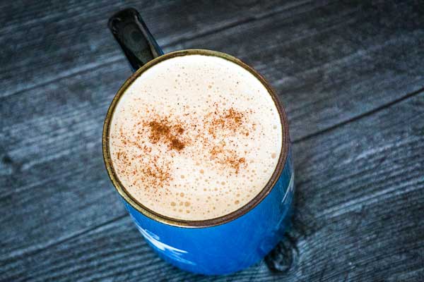 keto snickerdoodle coffee in a blue mug with cinnamon sprinkled on top of the coffee