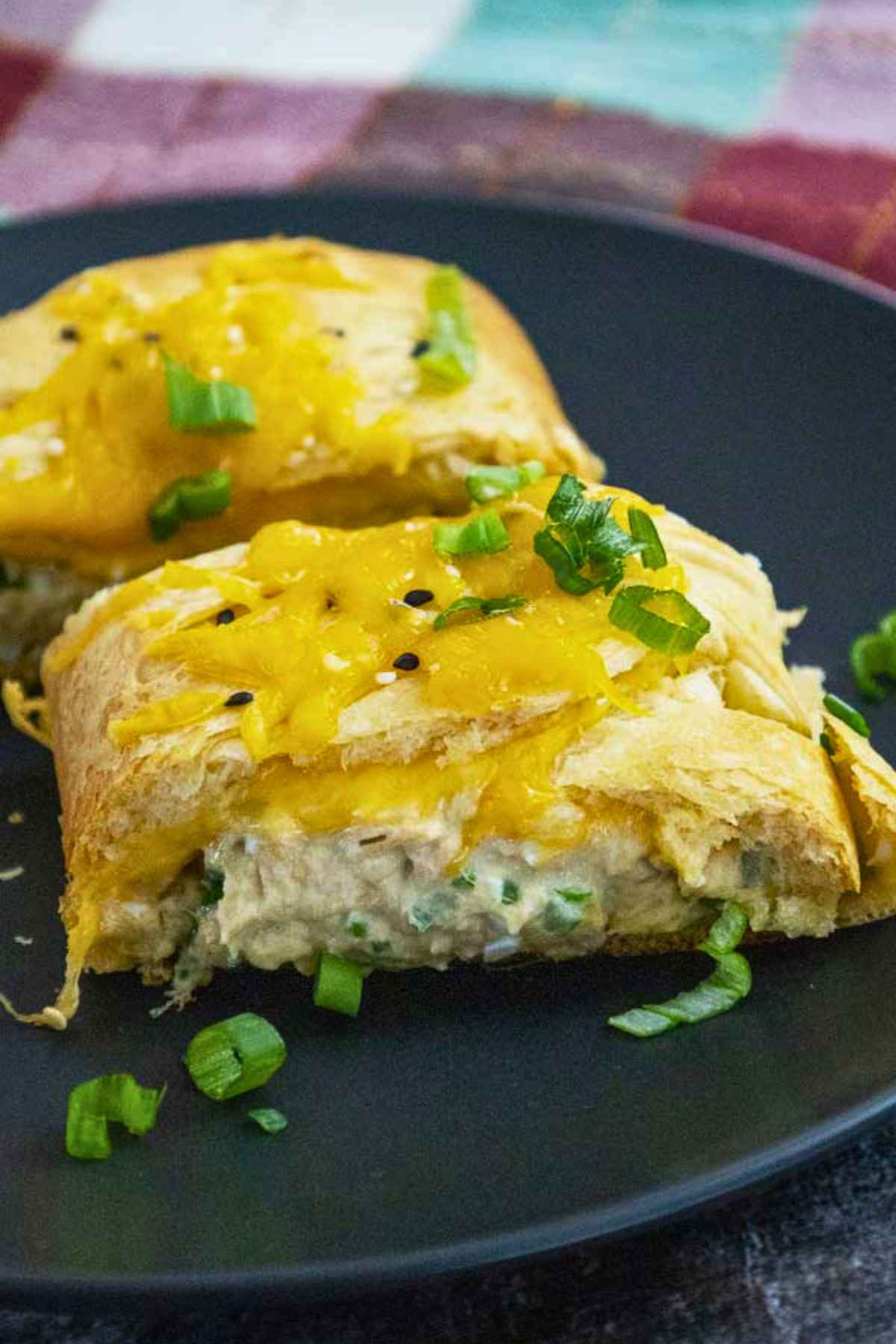 Sliced tuna crescent braid on a black plate with melted cheese topping and green onion garnish.