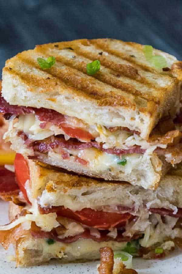 A close-up of two halves of a Bacon Tomato Grilled Cheese sandwich stacked together, showing melted cheese, crispy bacon, and fresh tomato slices on grilled artisan bread.