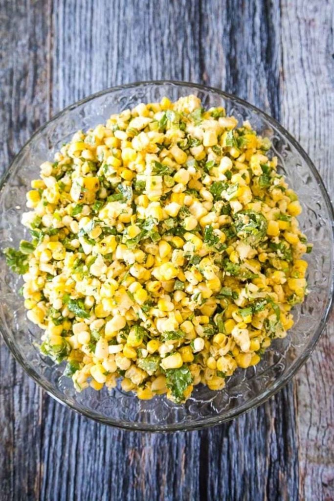 Mexican Street Corn Salad in a glass bowl with yellow grilled corn, green jalapeno, scallions, and cilantro.