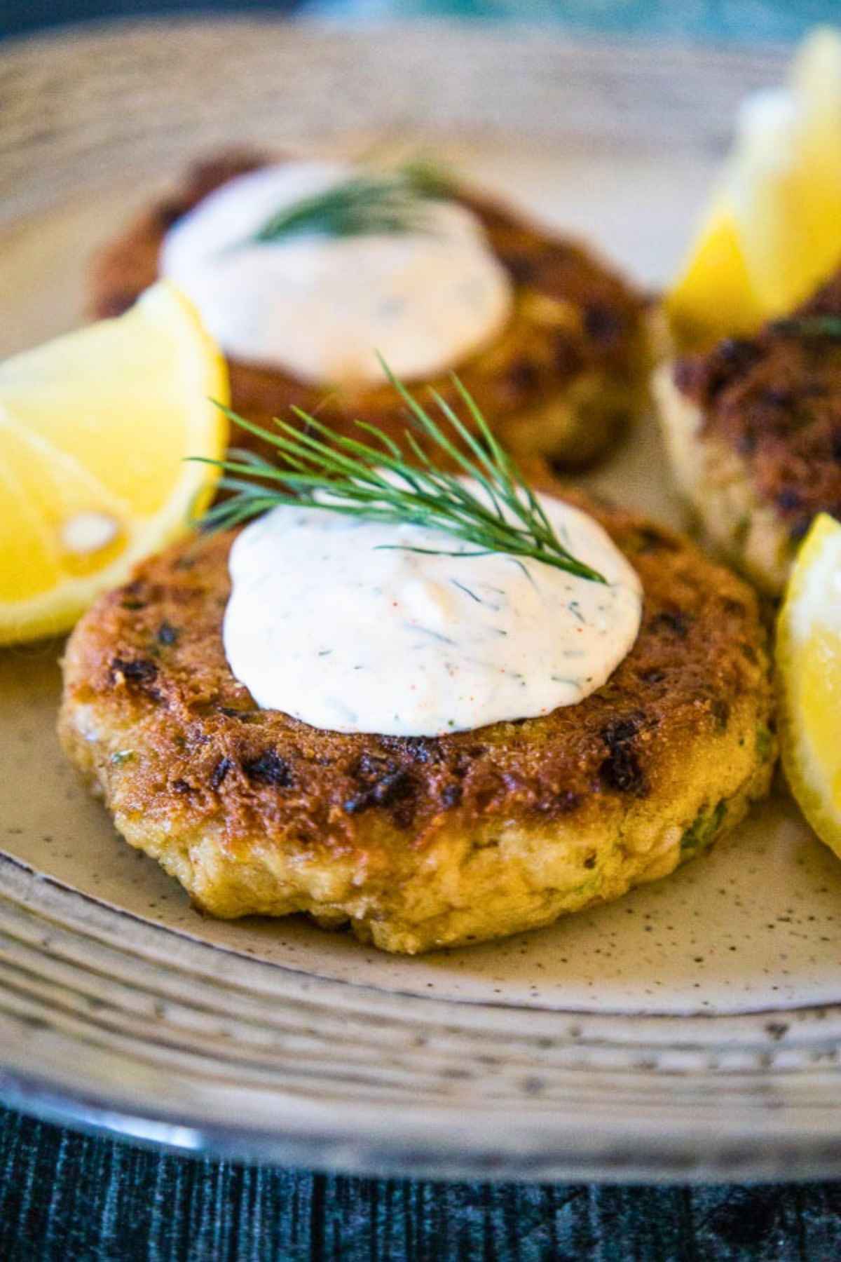 Golden brown salmon patties topped with creamy dill sauce and a sprig of fresh dill fronds.