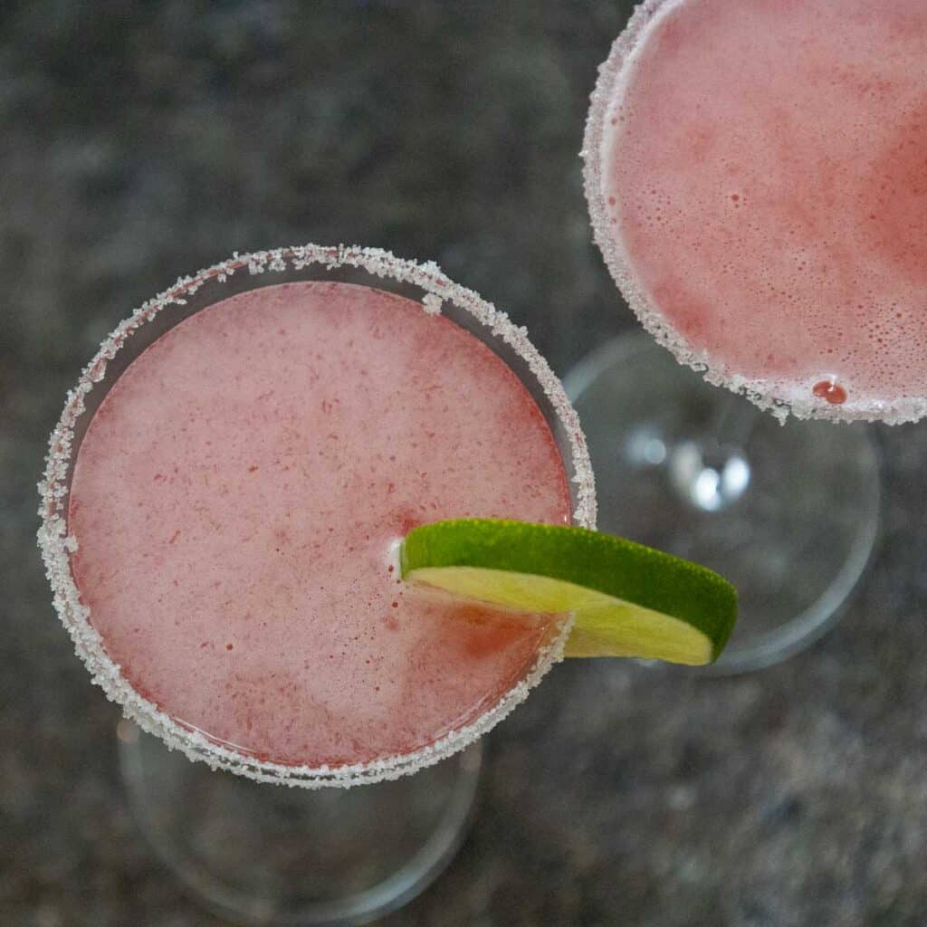 overhead shot of two light pink martinis with a sugar rim and green lime wedge on the forward martini.