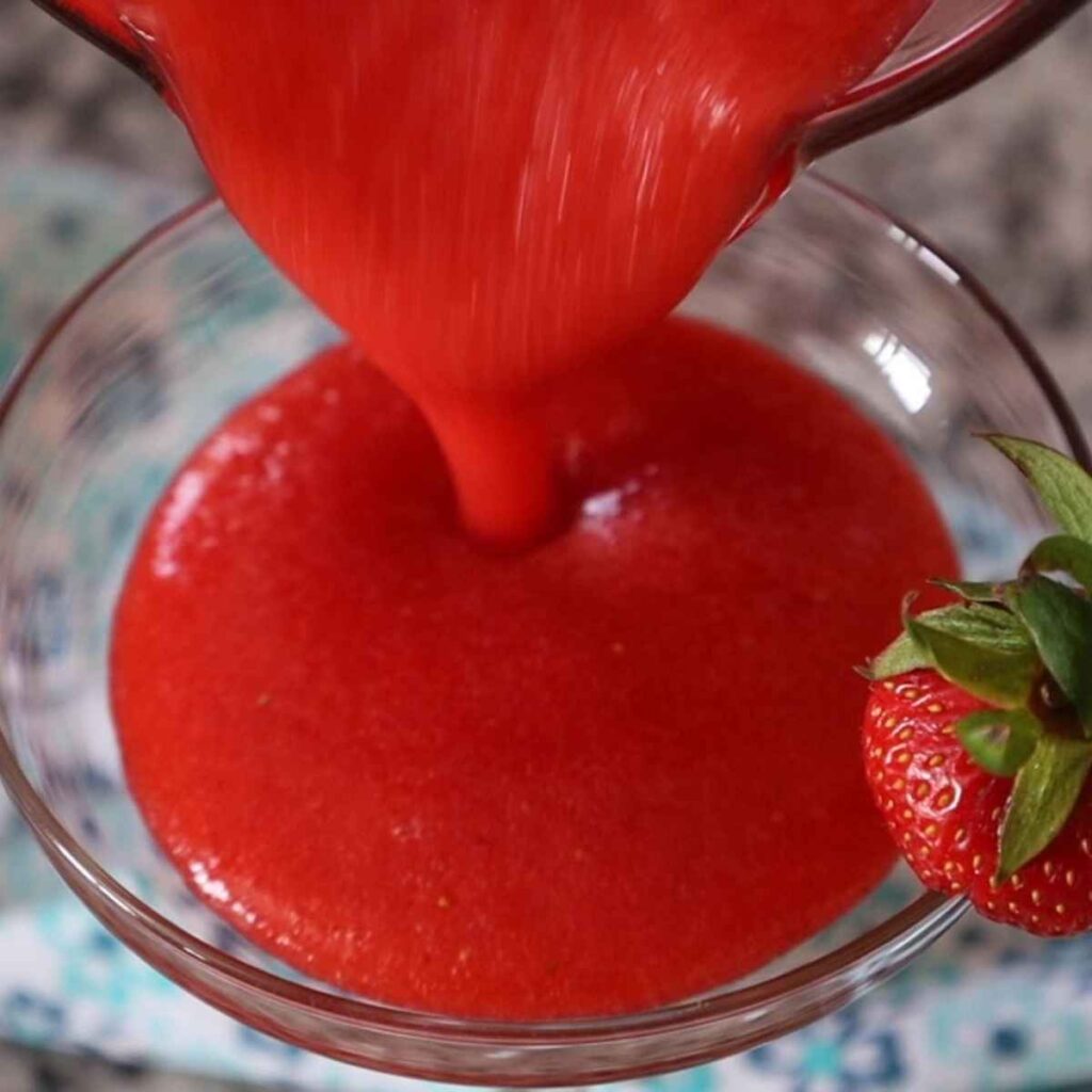 Pouring the red slushy drink from the bender into a daiquiri glass.