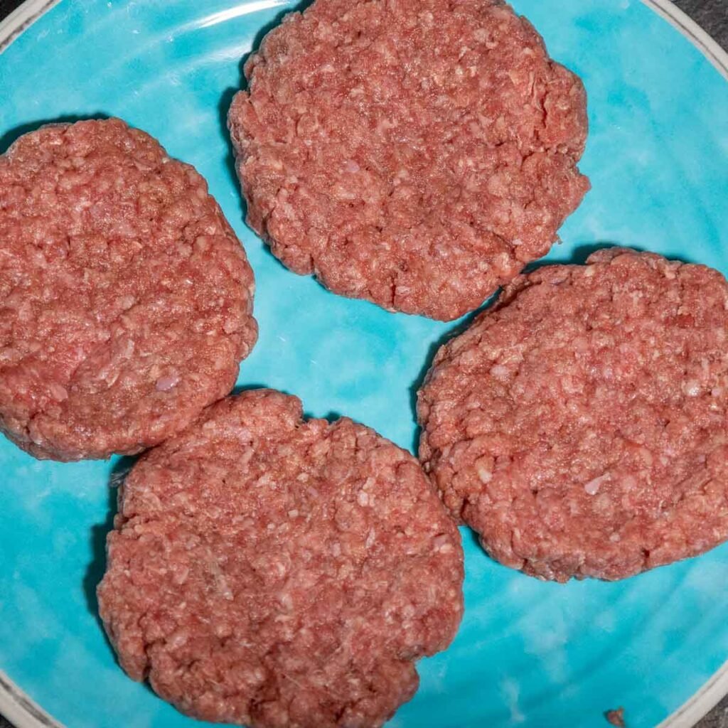 Four raw ¼lb burgers shaped and on a blue plate.