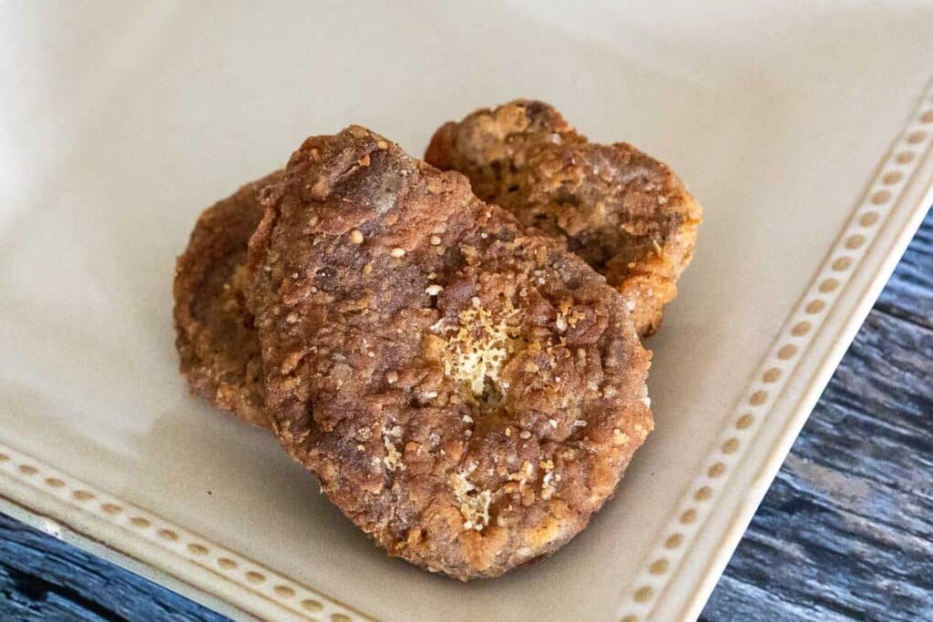 Three country fried vegan steaks on a cream colored plate.