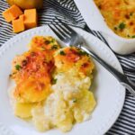 Close up of a white plate with a hearty serving of scalloped potatoes, featuring a golden cheesy crust and creamy interior, sprinkled with fresh parsley.