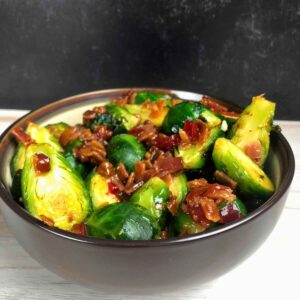 Side view of a brown and serving bowl filled with crispy air-fried pepper jelly Brussels sprouts topped with crumbled bacon.