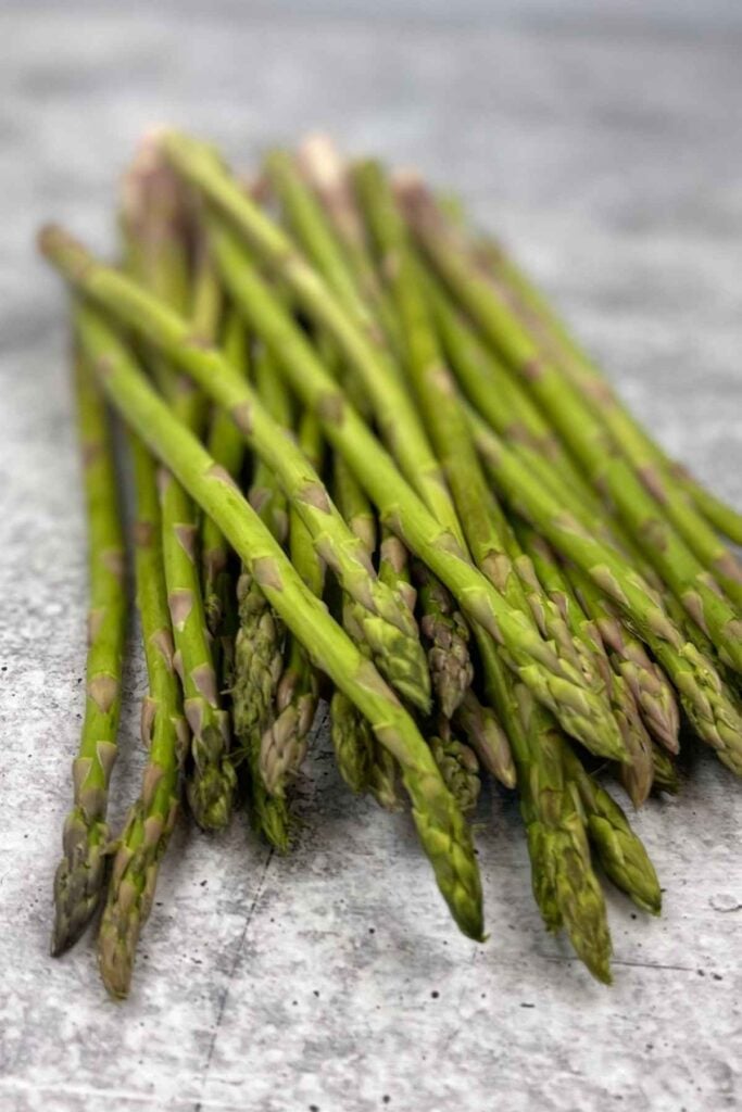 Whole raw asparagus spears on a gray marble counter.
