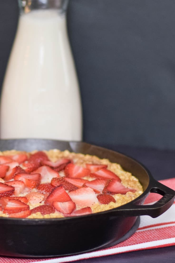 Strawberry Baked Oatmeal in a cast iron skillet with sliced strawberries on top and a milk jug in the background.