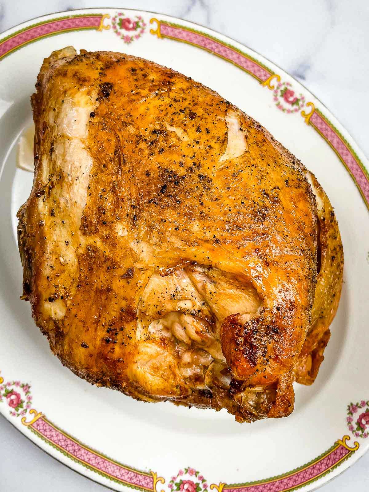 Sliced cooked turkey breast on a vintage floral patterned serving platter showing juicy interior and golden brown crispy skin.