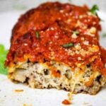 Close up of a sliced vegetarian meatball on a plate, revealing a cheesy and hearty interior beneath marinara sauce.