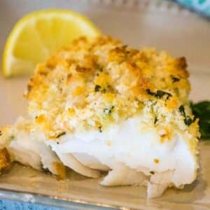 Oven baked haddock on a plate with a lemon wedge.