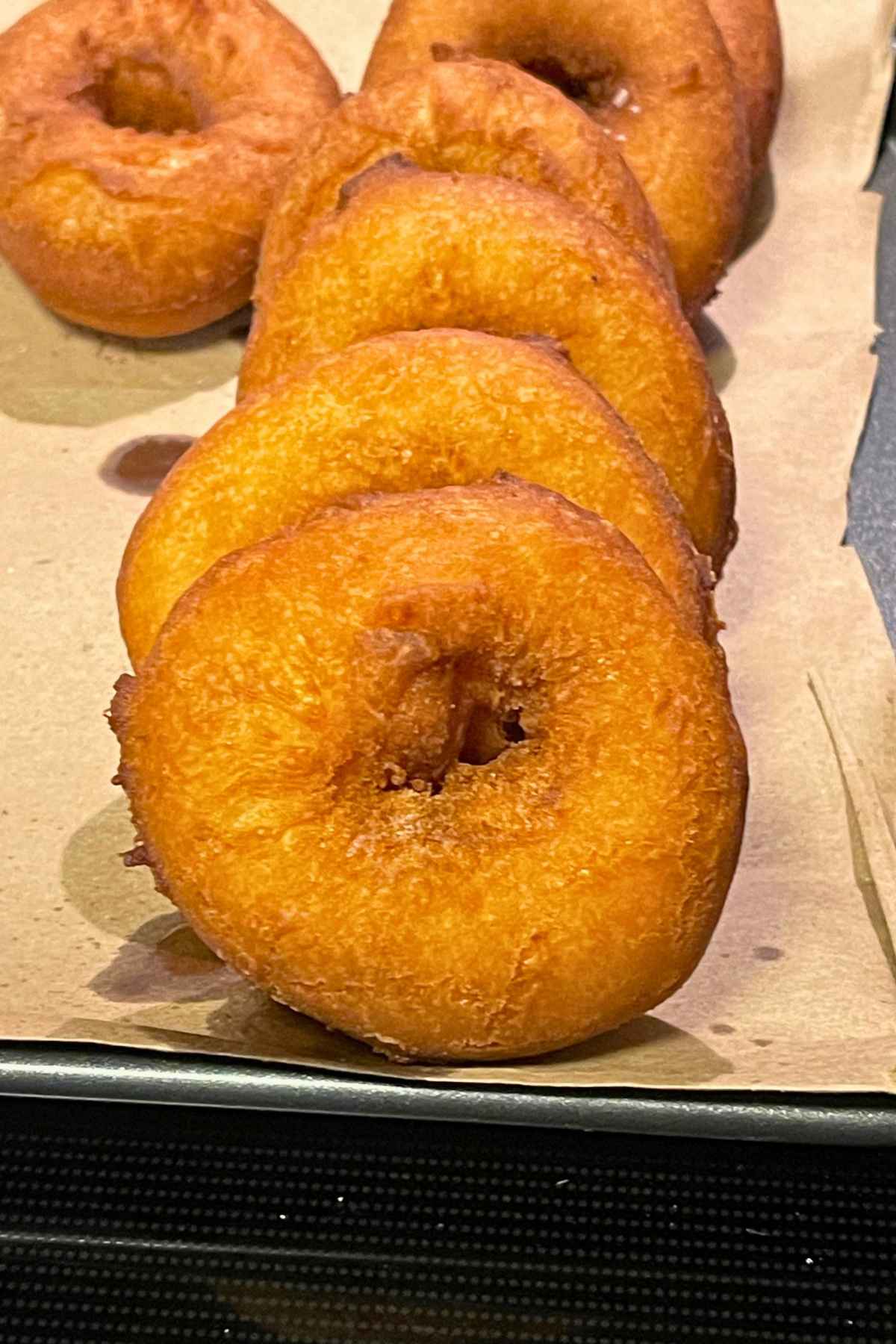 Fried buttermilk donuts cooling on a paper lined baking sheet.