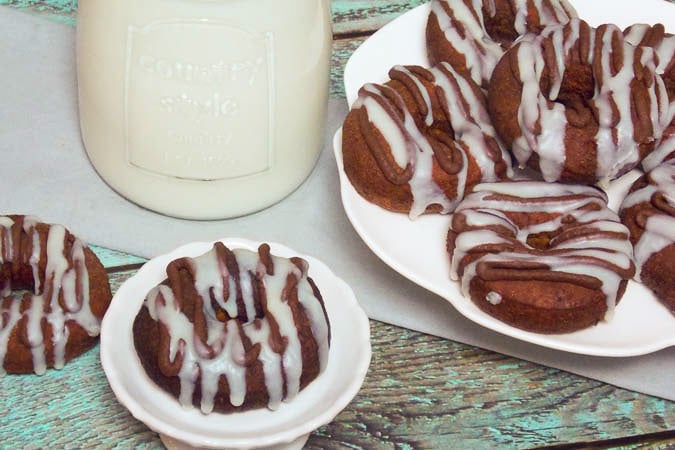 Fried chocolate doughnuts on a plate with white and dark chocolate drizzle.