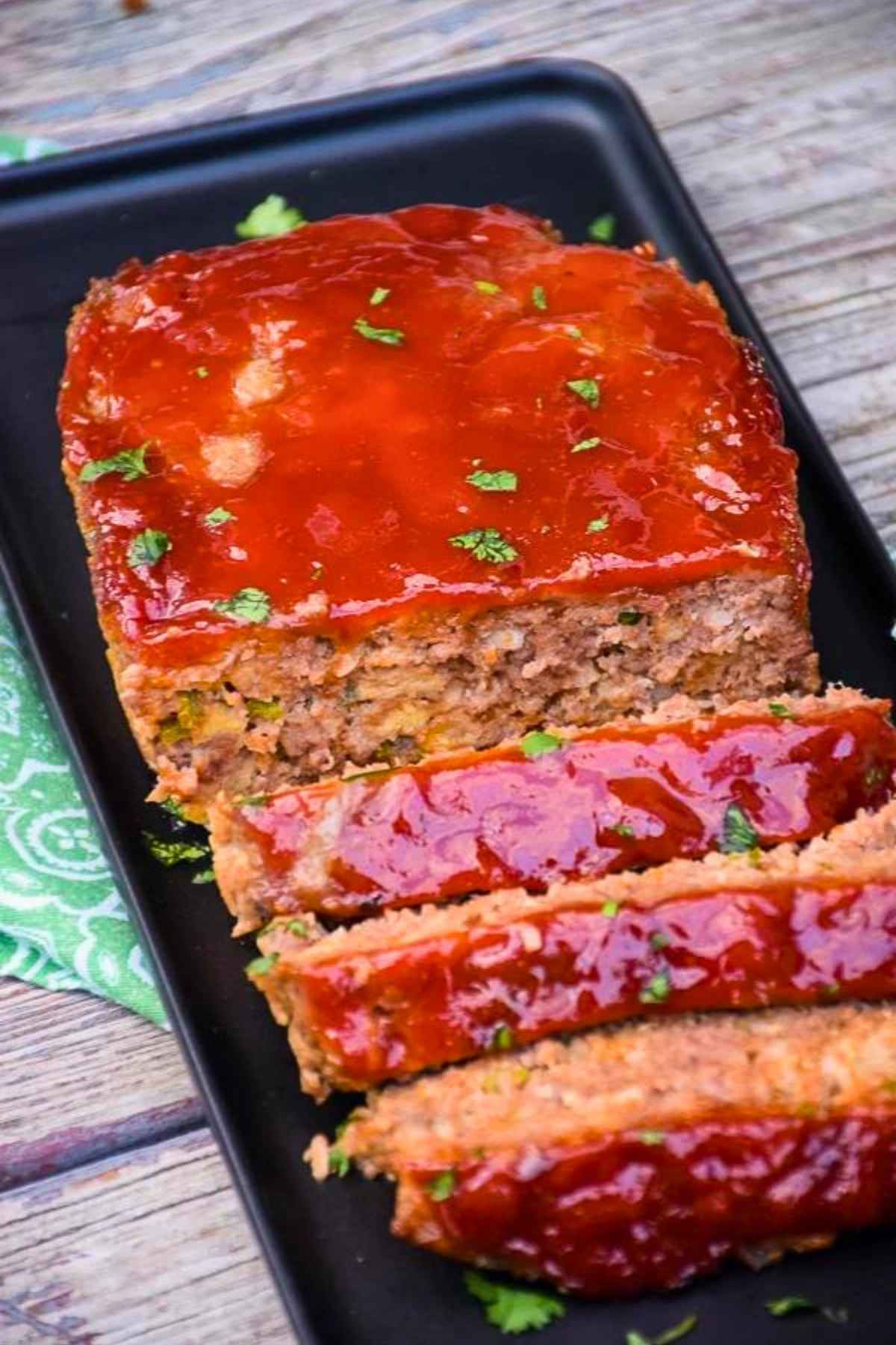 Cooked spicy jalapeno popper meatloaf on a black tray with cut slices.