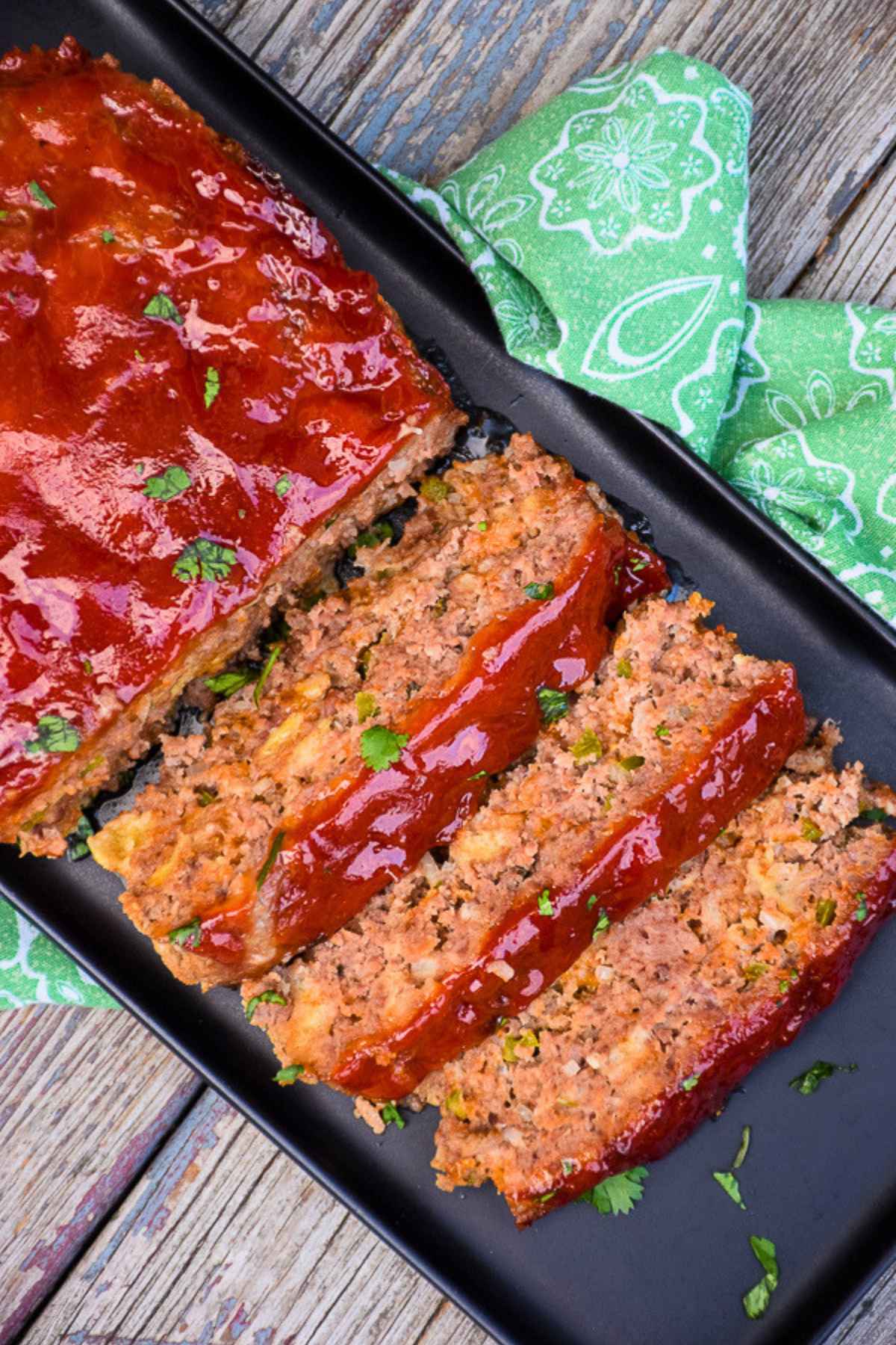 Overhead image of Cheddar Jalapeno Meatloaf on a black serving tray with 3 slices cut from the loaf.