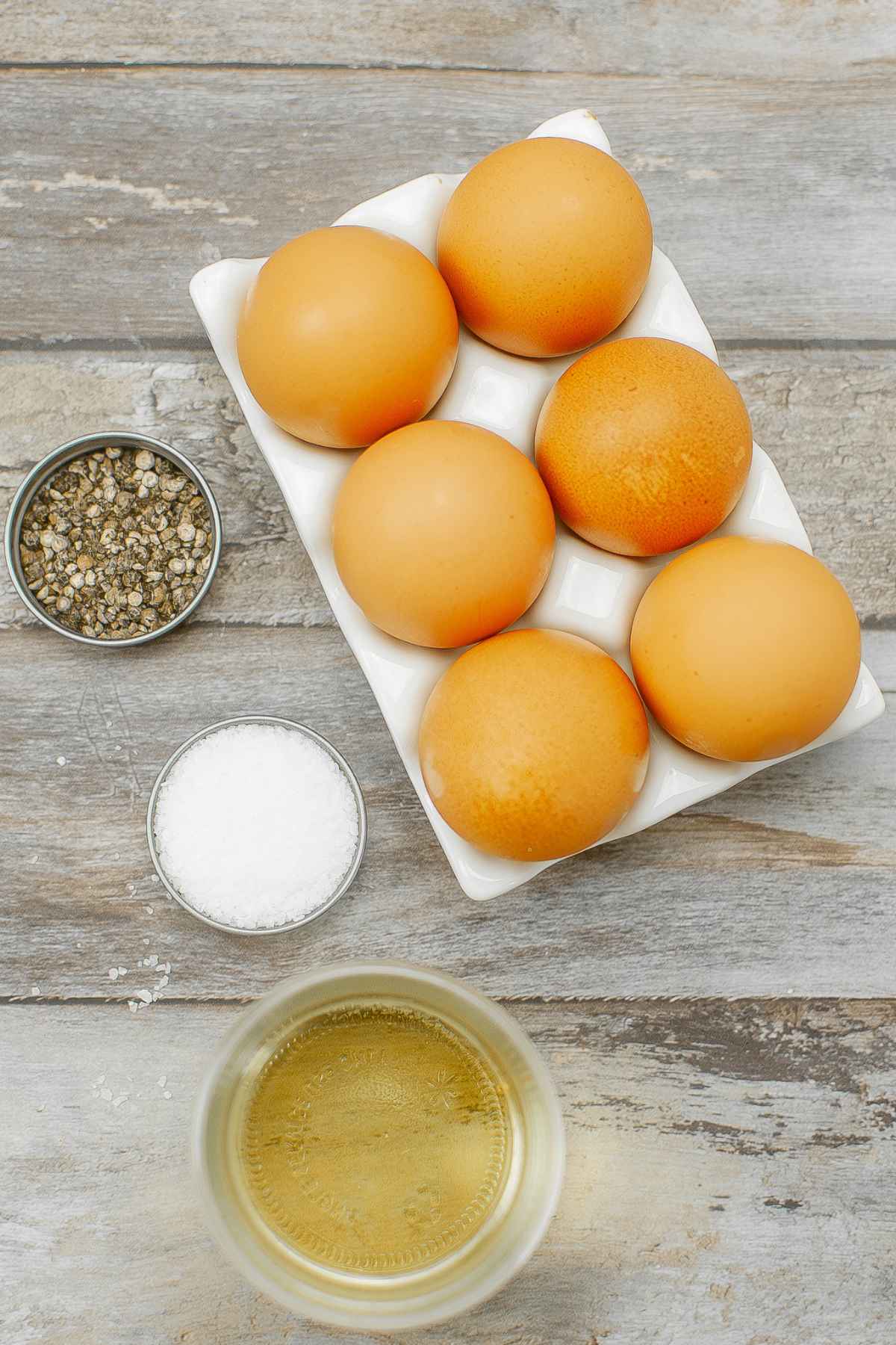 Six eggs, salt, pepper, and oil on a wooden pallet.