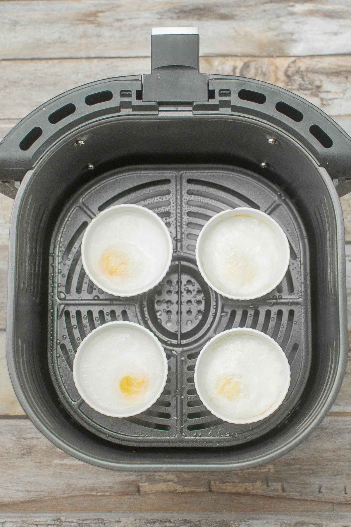 Four ramekins with cooked eggs in the air fryer basket.