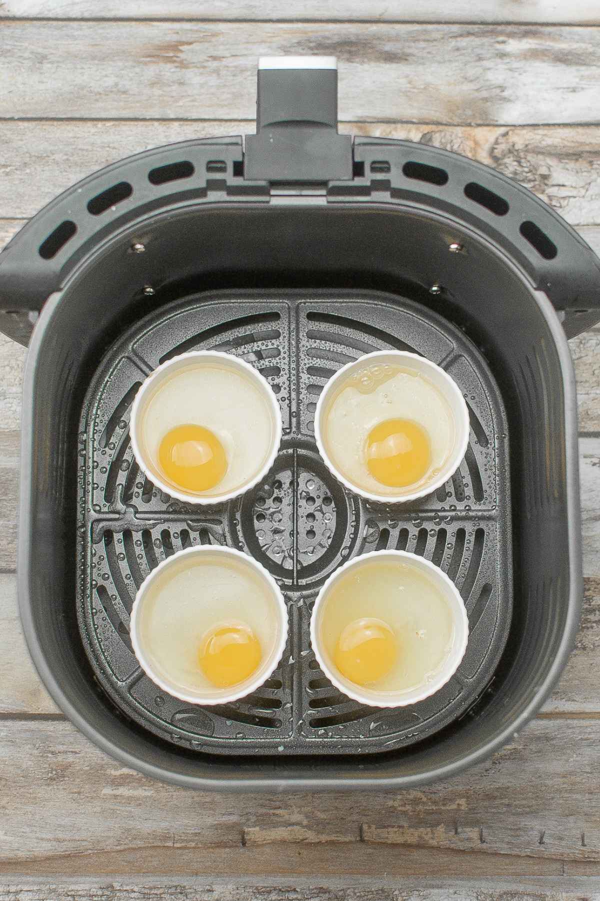 Raw eggs in boiling water in ramekins in basket.