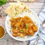 A bowl of slow cooker butter chicken on a bed of jasmine rice and a side of naan bread.