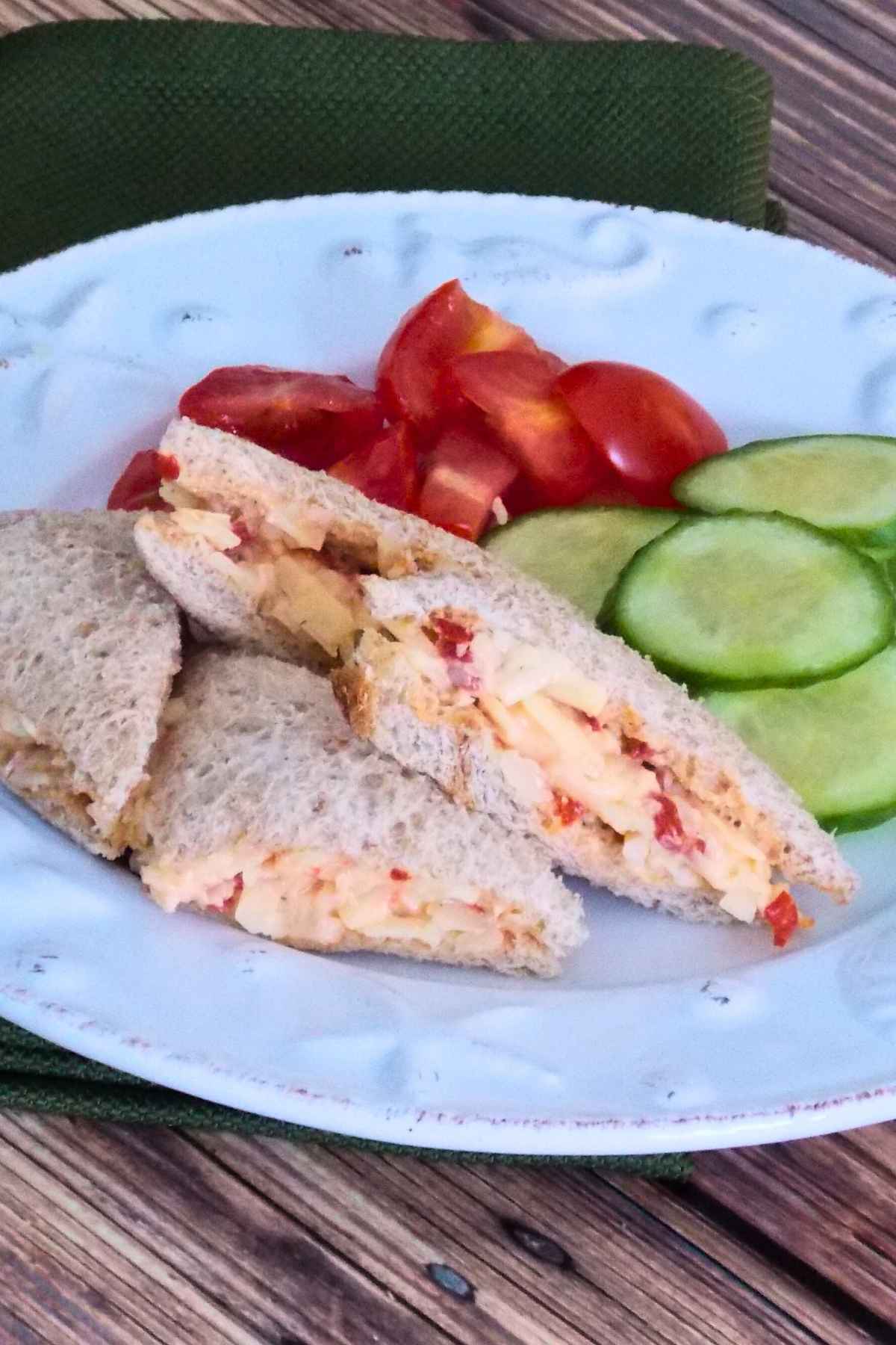 Pimento Cheese Tea Sandwiches on a seashell plate with a side of sliced cucumbers and tomatoes.