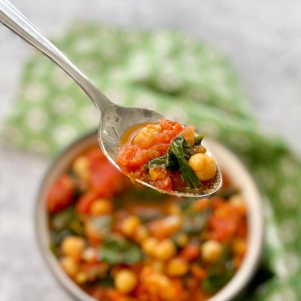 A serving of chickpea, spinach and tomato curry on a silver spoon.