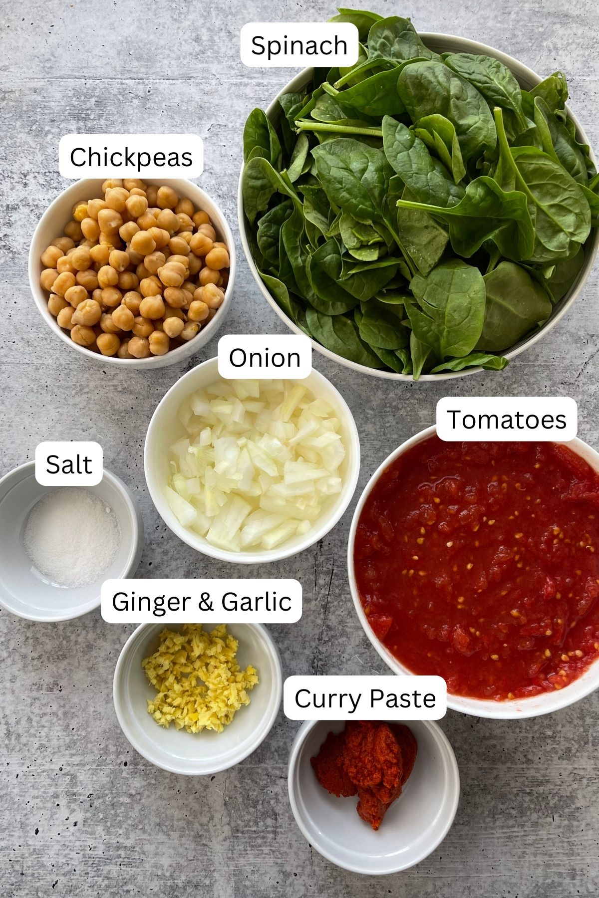 Recipe ingredients in bowls: spinach, tomatoes, curry paste, ginger, garlic, onion, salt, and chickpeas.
