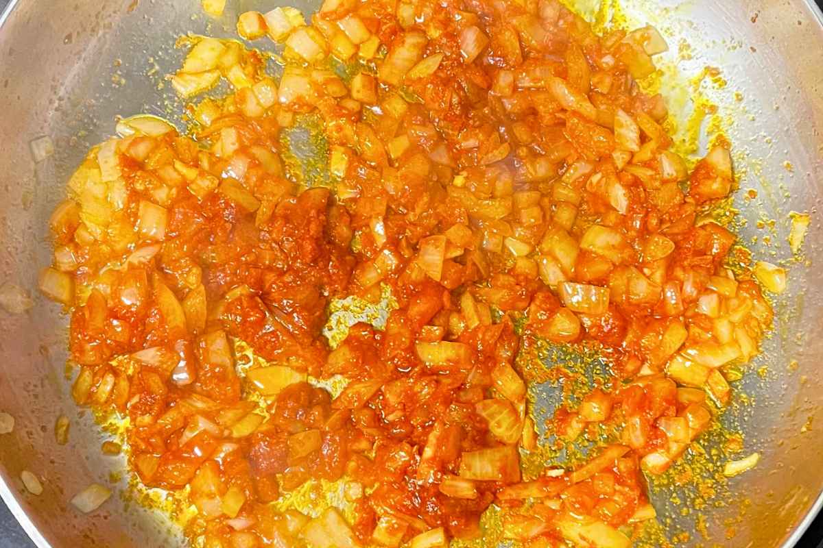 Onion and red curry mixture in a stainless steel skillet.
