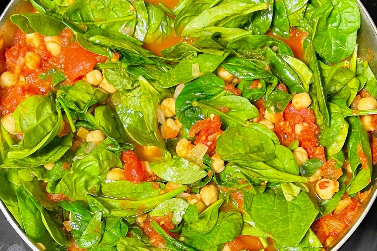 Spinach added to chickpea and tomato mixture in skillet.