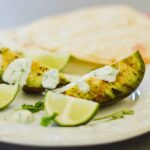 Grilled Avocado slices on a plate topped with cilantro lime cream with lime wedges for garnish.
