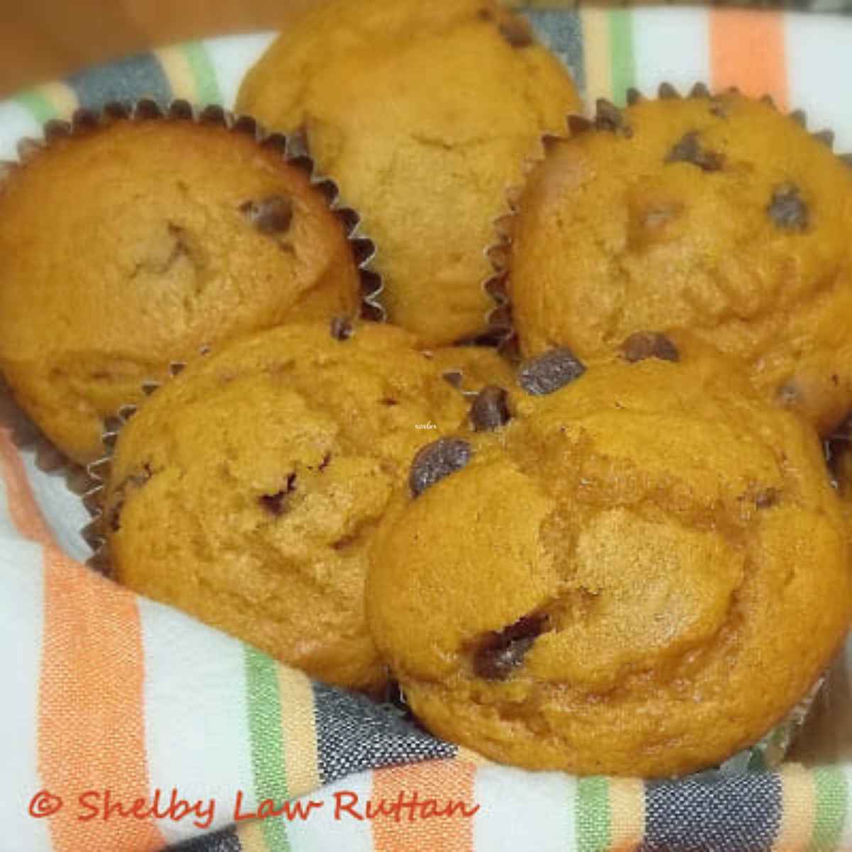 A orange striped towel lined basket filled with low fat pumpkin chip muffins.