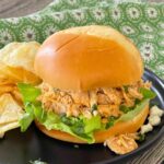 Slow Cooker Buffalo Chicken shredded on a roll with lettuce, blue cheese, and cilantro.
