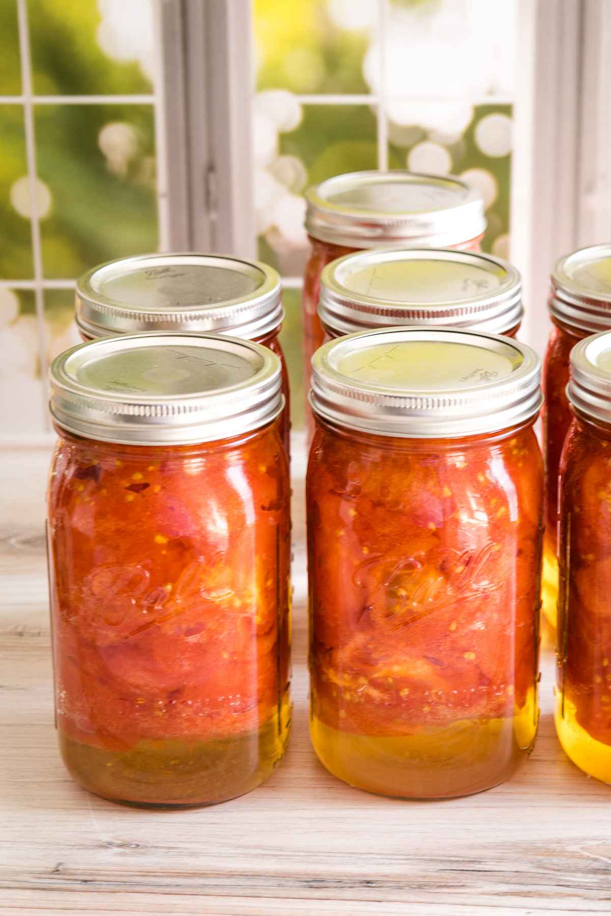 Several quart jars of canned tomatoes in a window sill.