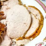 Sliced cooked turkey breast on a vintage floral-patterned serving platter, showing juicy interior and golden brown crispy skin.