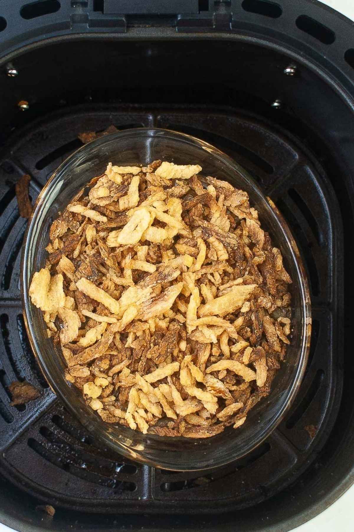 Overhead view of a glass baking dish filled with casserole topped with crispy fried onions, placed inside the basket of an air fryer.