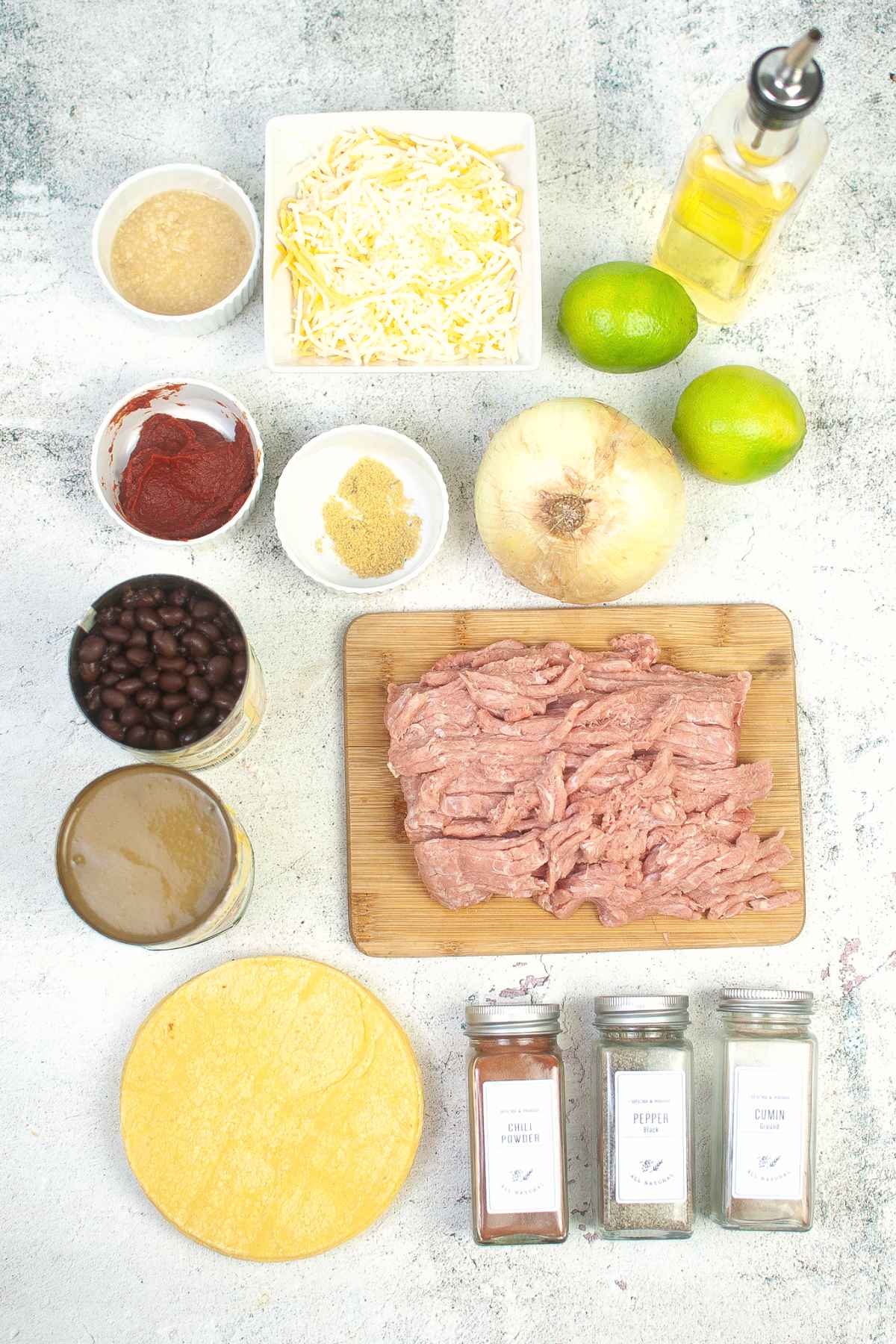 Overhead view of ingredients including tortillas, shredded turkey, cheese, black beans, spices, lime, and onion.