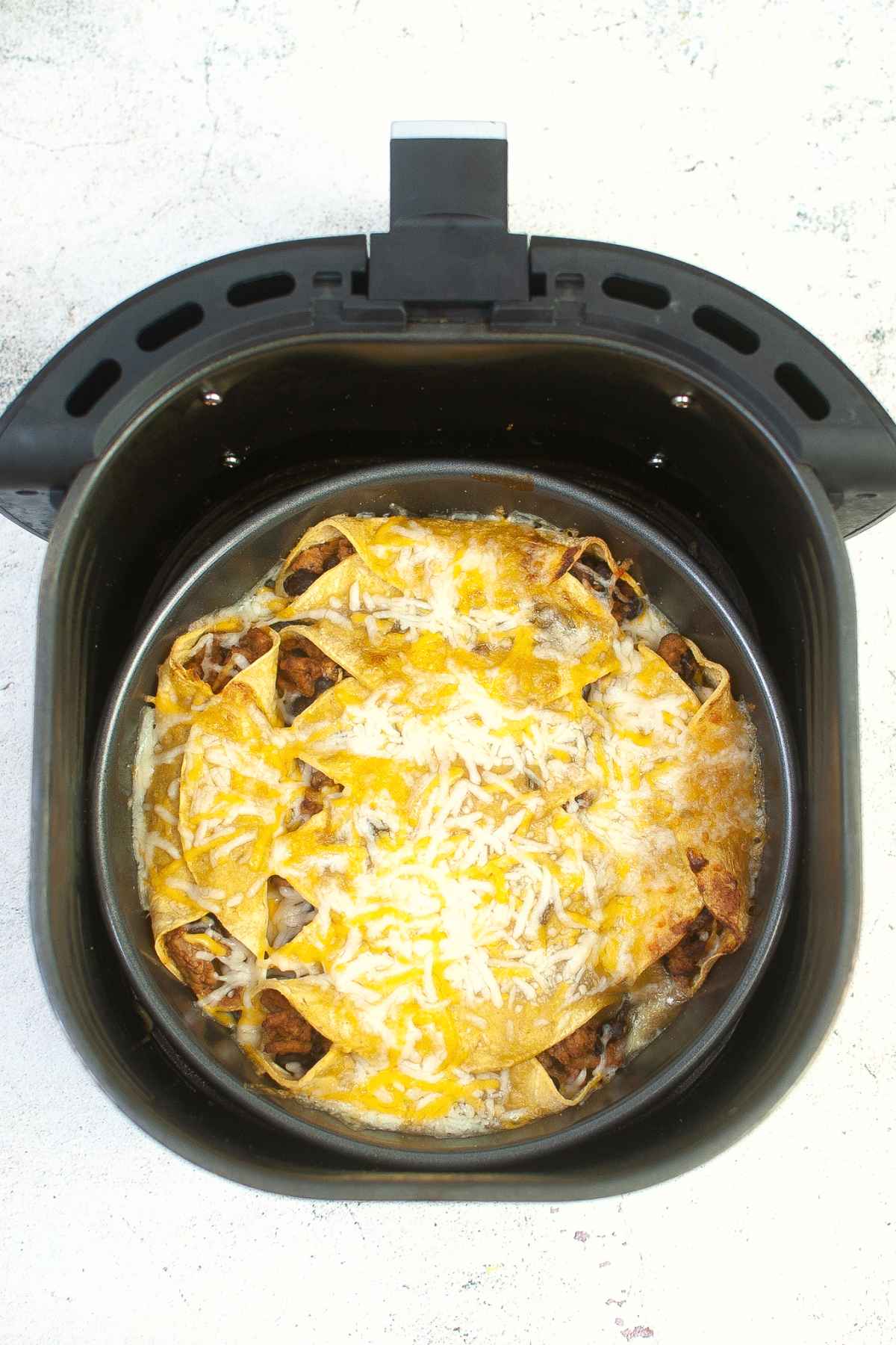 Overhead view of turkey black bean enchiladas inside an air fryer basket with melted cheese on top.
