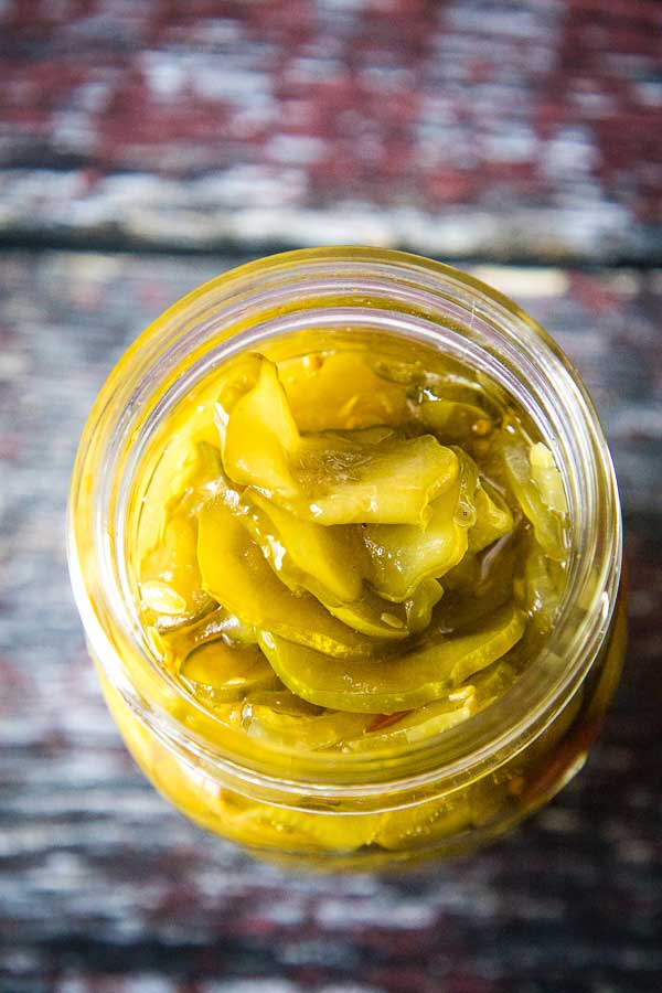 Overhead view of an open jar filled with bread and butter pickles, showing thick, glossy pickle slices inside.
