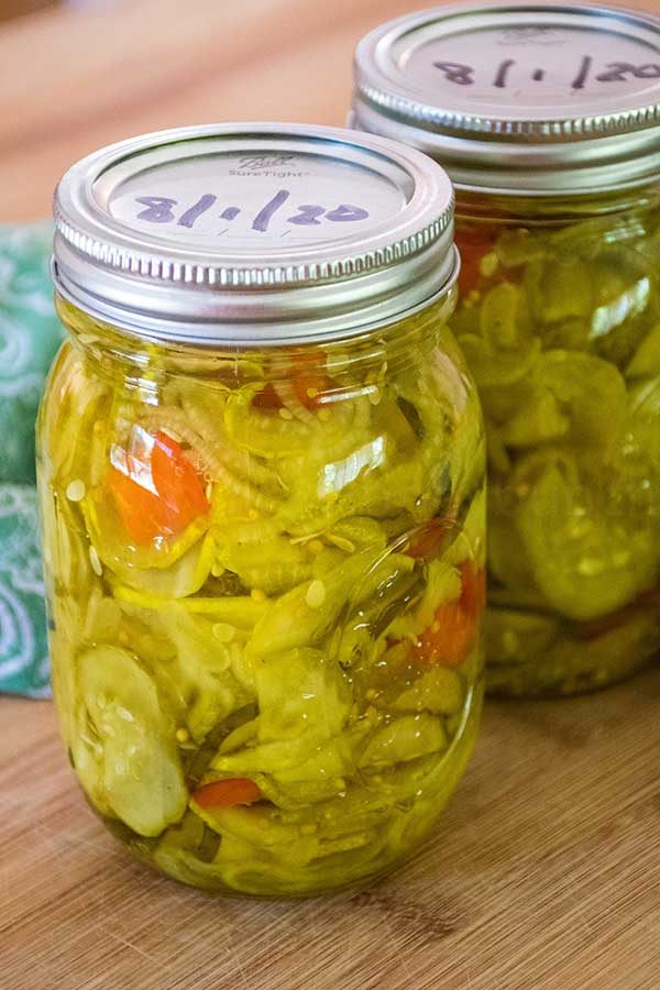 Close-up of two sealed jars of pickles on a wooden surface, showcasing the vibrant yellow brine and vegetables inside.