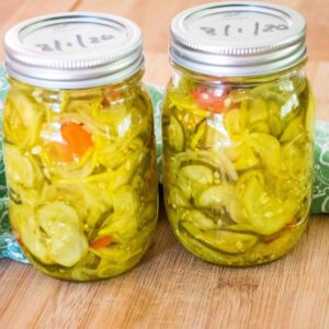 Two jares of homemade bread and butter pickles filled with sliced cucumbers, onions, and red peppers, sealed and dated on the lids.