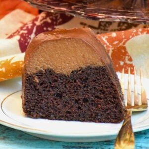 One slice of triple chocolate mousse bundt cake on a white plate with a gold fork and fall themed napkin.