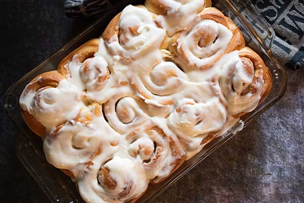 Overhead view of a glass baking dish filled with freshly baked cinnamon rolls, generously topped with creamy icing.